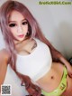 A woman with long pink hair wearing a white tank top.