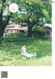 A woman sitting on the grass in front of a tree.