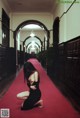 A woman in a black dress crouching down on a red carpet.