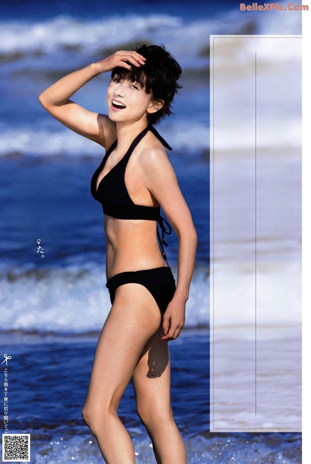 A woman in a black bikini standing on the beach.