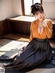 A woman in a black and orange dress sitting on a tatami mat.