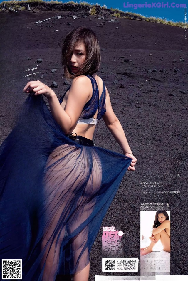 A woman in a blue dress standing on a black sand beach.