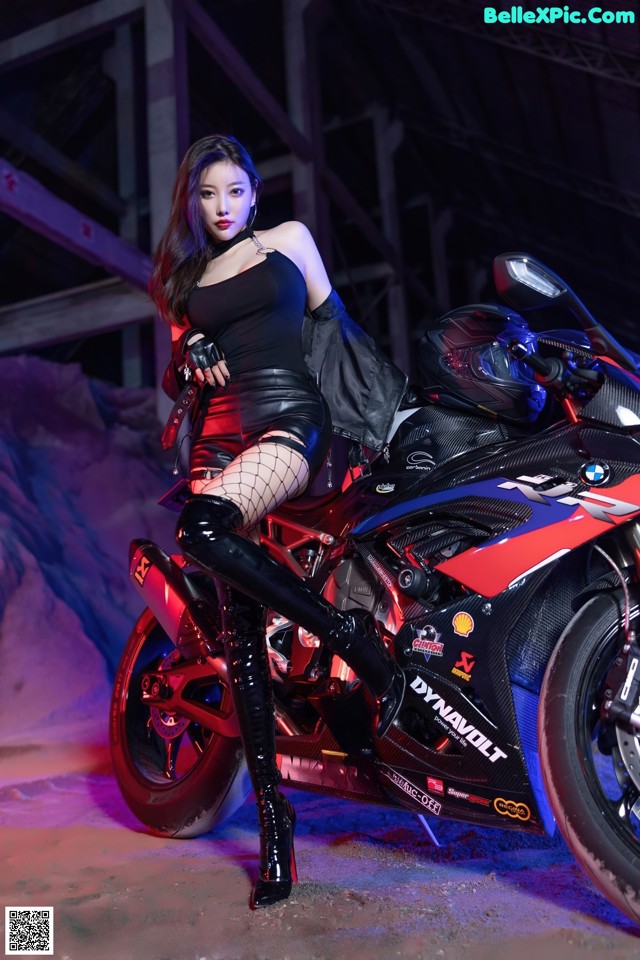 A woman in a black dress sitting on a motorcycle.