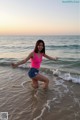 A woman in a pink tank top and denim shorts standing in the ocean.