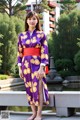 A woman wearing a purple and yellow kimono standing in front of a pond.