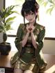 A woman in a green kimono sitting on a table next to a plant.