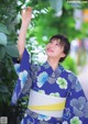 A woman in a blue and white kimono standing next to a tree.