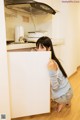 A woman crouching down in a kitchen next to a refrigerator.