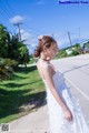 A woman in a white dress standing on the side of a road.