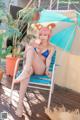 A woman in a bikini sitting on a deck with an umbrella.